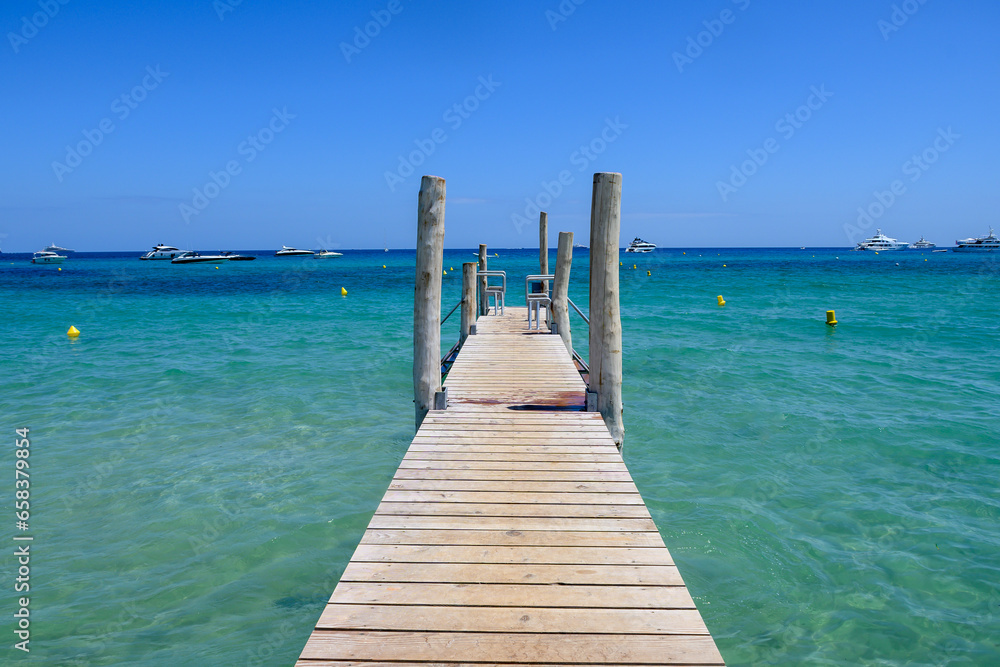 Wooden pier and crystal clear blue water of legendary Pampelonne beach near Saint-Tropez, summer vacation on French Riviera, France