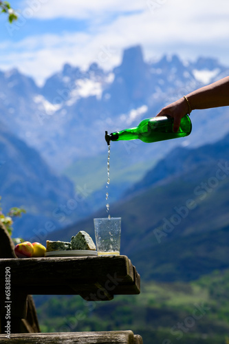 Pouring from high height of natural Asturian cider made from fermented apples, Asturian cabrales cow blue cheese with view on Naranjo de Bulnes top of Picos de Europa mountains, Spain