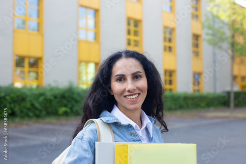 Shoulder length portrait of a high school girl walking to class with folders in her hands and backpack, turned and smiling, looking at camera, happy to be back at school. Educational institution.