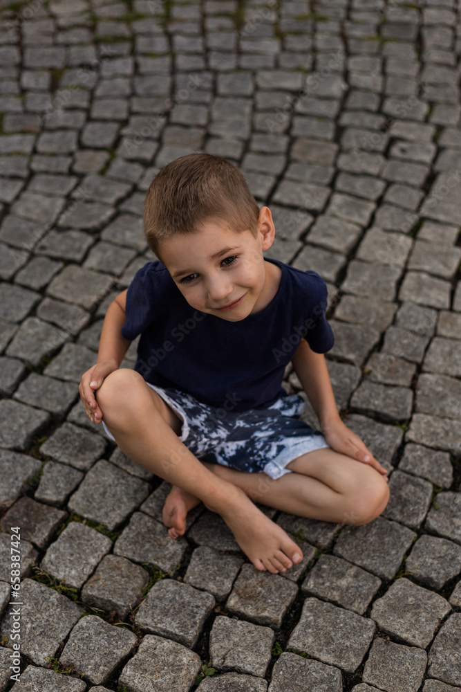 Boy is sitting on the sidewalk. Children's upbringing, freedom. Child is playing