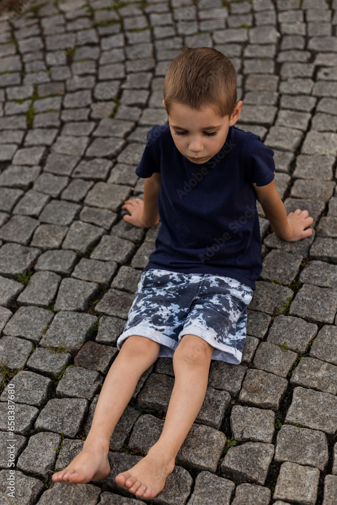 Sad offended boy sitting on the sidewalk. Children's emotions and upbringing Sad offended boy sitting on the sidewalk. Children's emotions and upbringing