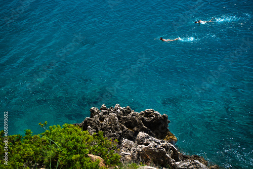 Steep rocky coast with swimmers in the sea