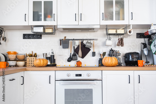 Decor of the white classic kitchen with pumpkins for Halloween and harvest. Autumn mood in the home interior, modern loft style.