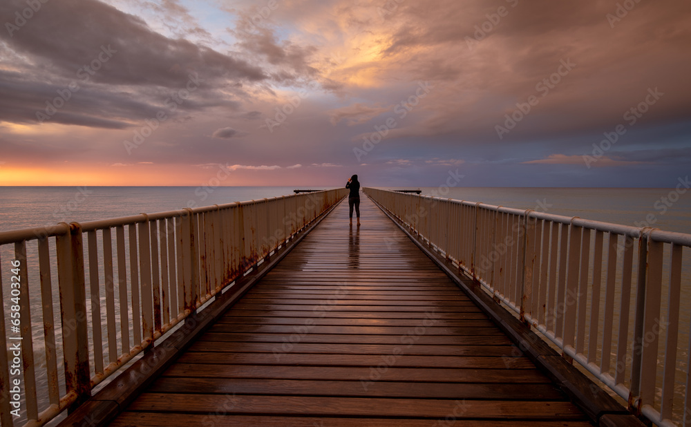 Person standing alone on a pier enjoying dramatic sunset at the sea. Exploring nature. Dramatic light