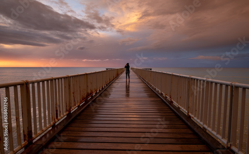 Person standing alone on a pier enjoying dramatic sunset at the sea. Exploring nature. Dramatic light © Michalis Palis