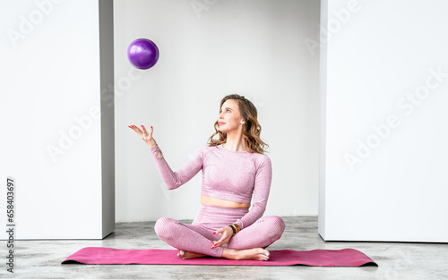 Slim woman with rubber ball rubber ball for rhythmic gymnastics. Training yoga in pink tight-fitting tracksuit in fitness gym. Stretching, pilates practice. Workout, exercises at home on fitness mat