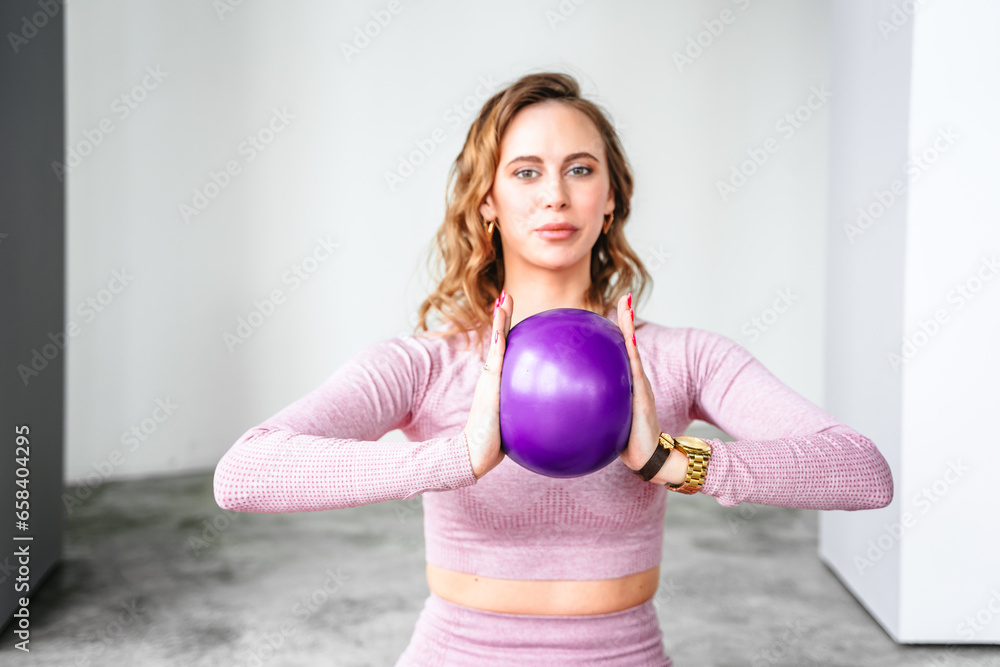 Slim woman with rubber ball rubber ball for rhythmic gymnastics. Training yoga in pink tight-fitting tracksuit in fitness gym. Stretching, pilates practice. Workout, exercises at home on fitness mat Slim woman with rubber ball rubber ball for rhythmic gymnastics. Training yoga in pink tight-fitting tracksuit in fitness gym. Stretching, pilates practice. Workout, exercises at home on fitness mat