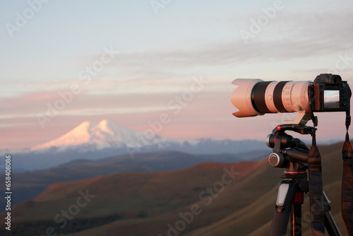Evening photography. Camera with a long lens on a tripod. Snow-covered volcano peak in the background.