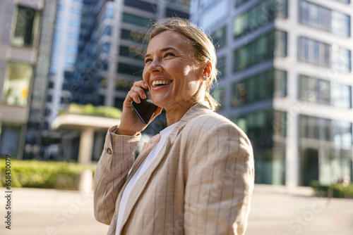 Close up of female manager talking phone standing on modern office building background