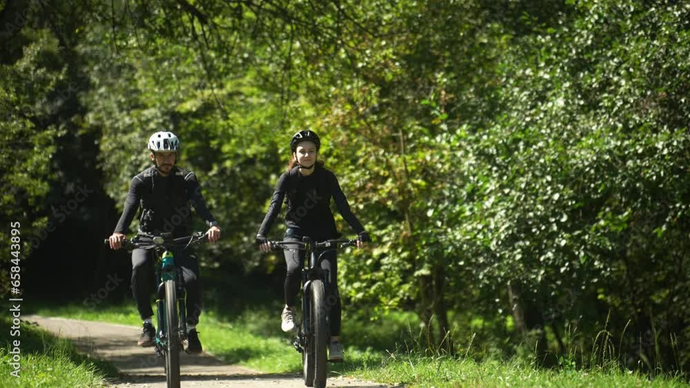 Young Couple Rides a Bicycle in the Park Without Pedaling. Concept of Healthy lifestyle, Spring or Summer Activity, Happy Relationship, Active Life, Bonding, Weekend Activity, Friendship, Recreation Young Couple Rides a Bicycle in the Park Without Pedaling. Concept of Healthy lifestyle, Spring or Summer Activity, Happy Relationship, Active Life, Bonding, Weekend Activity, Friendship, Recreation