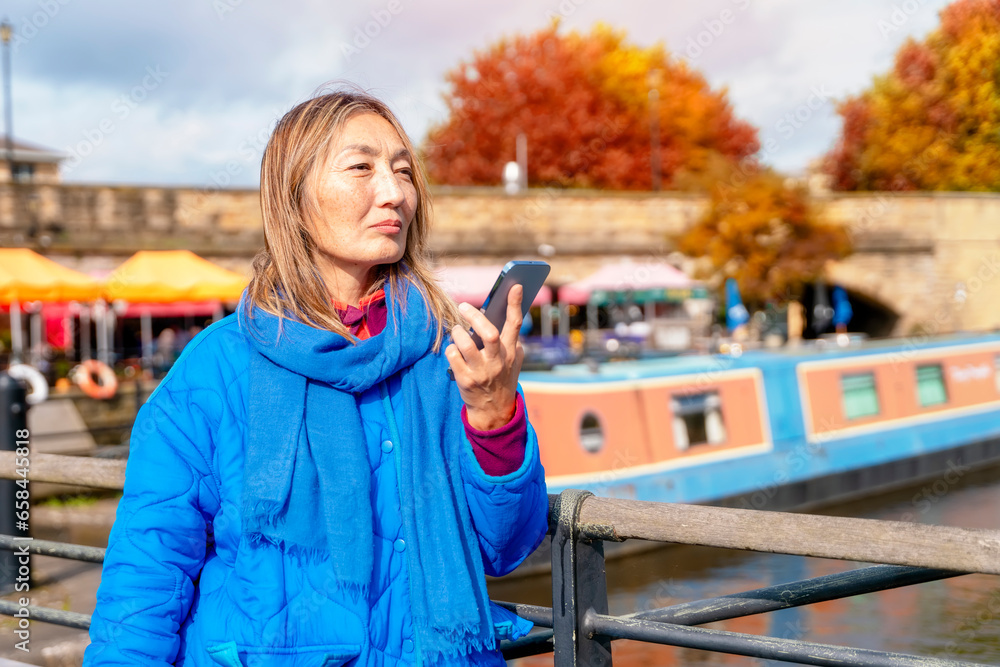 asian woman in blue jacket and glasses walking on the quays, pier, sitting on bench, looking at yacht, sailboat, boat, using phone. Lifestyle travel concept