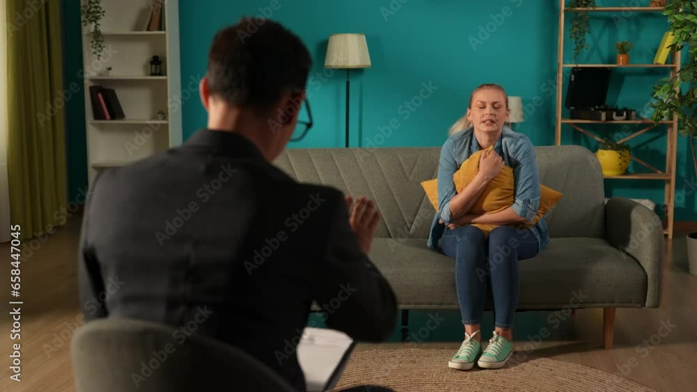 A male psychologist works with an unhappy woman suffering from depression. The woman sits on the couch in front of the specialist, hugging a cushion. Attending a psychotherapy session. A male psychologist works with an unhappy woman suffering from depression. The woman sits on the couch in front of the specialist, hugging a cushion. Attending a psychotherapy session.