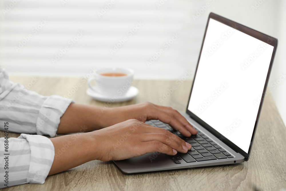 Woman using laptop at wooden desk indoors, closeup Woman using laptop at wooden desk indoors, closeup