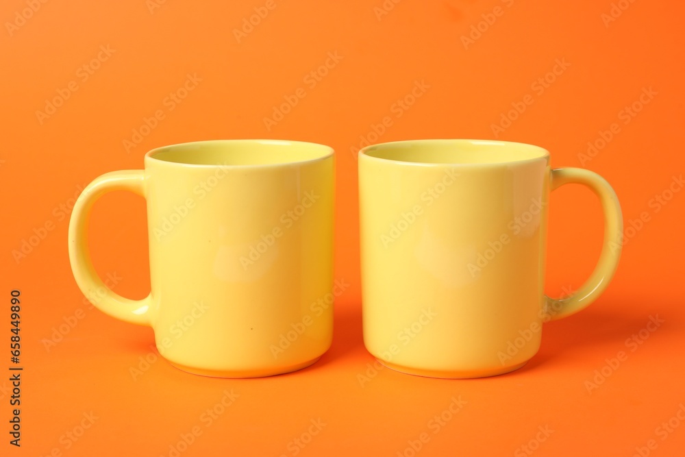 Two yellow ceramic mugs on orange background Two yellow ceramic mugs on orange background