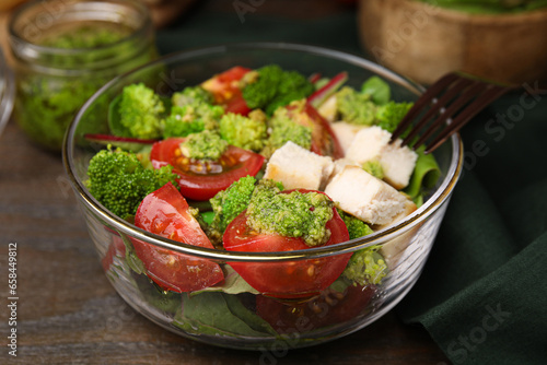 Delicious salad with pesto sauce in bowl and fork on table, closeup