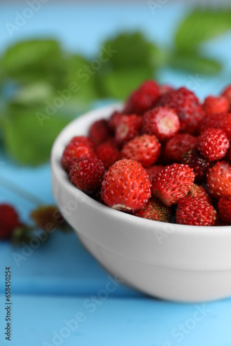 Fresh wild strawberries in bowl on light blue table, closeup