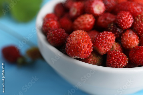 Fresh wild strawberries in bowl on light blue table  closeup