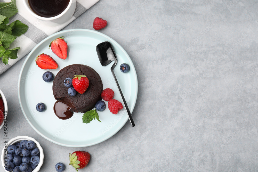 Plate with delicious chocolate fondant, berries and mint on grey table, flat lay. Space for text Plate with delicious chocolate fondant, berries and mint on grey table, flat lay. Space for text