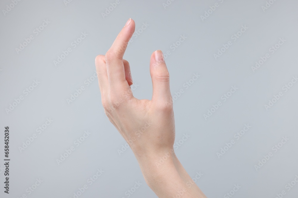 Woman holding something in fingers on grey background, closeup Woman holding something in fingers on grey background, closeup