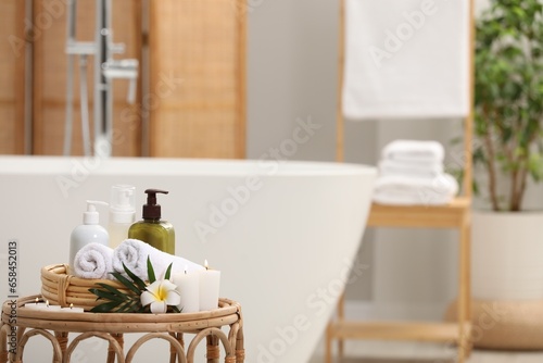 Spa products, burning candles, plumeria flower and tropical leaf on table in bathroom. Space for text