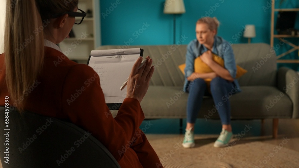 Female psychologist works with unhappy depressed woman, diagnoses problems. The woman sits on a couch in front of the specialist, hugging a pillow. Attending a session of psychotherapy. Female psychologist works with unhappy depressed woman, diagnoses problems. The woman sits on a couch in front of the specialist, hugging a pillow. Attending a session of psychotherapy.