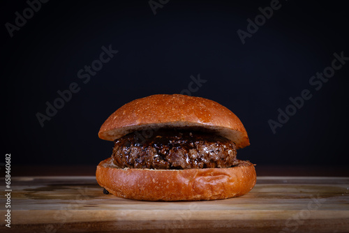 Beef burger with sauce served on cutting board on a black wooden table. Craft beef burger with french fries, hand made.