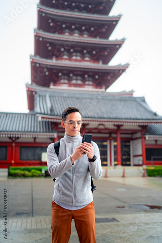 Hispanic tourist guy standing on blurred background of Japanese temple Sensoji  and sending text message via mobile phone during journey in Asakusa Tokyo, Japan photo