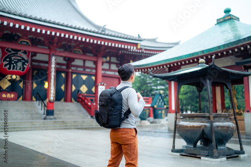 Back view full body of unrecognizable Hispanic tourist backpacker standing on street tiled pavement against entrance of Japanese Sensoji temple in Asakusa Tokyo, Japan