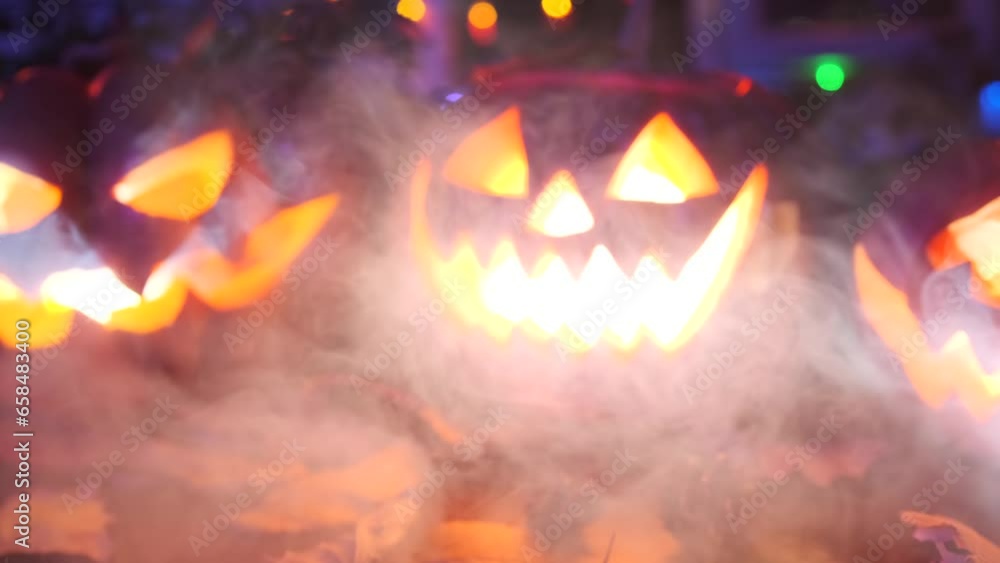 Jack-o'-lantern festive Halloween background. In thick cold fog, festive traditional carved pumpkins with candles inside flicker and glow lying on table among leaves and autumn decoration. Jack-o'-lantern festive Halloween background. In thick cold fog, festive traditional carved pumpkins with candles inside flicker and glow lying on table among leaves and autumn decoration.