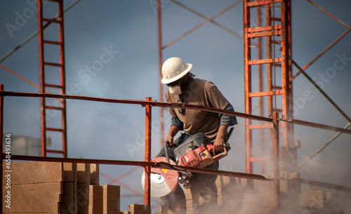 Construction worker wearing a hard hat operating a circular saw ar a job site with metal framing