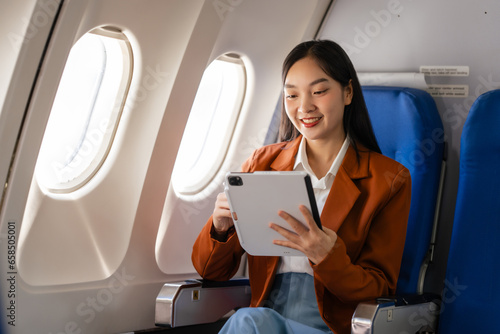 using tablet pc, Elegantly dressed brown suit Asian chinese japanese people businesswoman immersed in work, comfortably seated onboard, capturing the merging worlds of corporate hustle