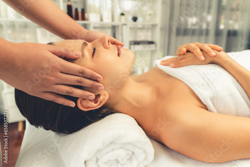 Caucasian woman enjoying relaxing anti-stress head massage and pampering facial beauty skin recreation leisure in dayspa modern light ambient at luxury resort or hotel spa salon. Quiescent