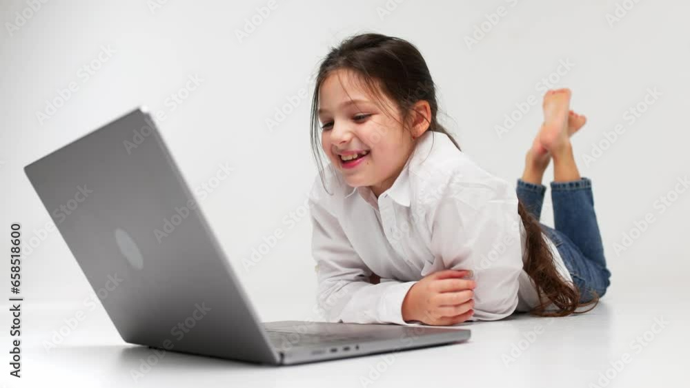 The concept of childish, sincere emotions. A little girl lies on the floor against a light background and watches a movie. Happy childhood concept The concept of childish, sincere emotions. A little girl lies on the floor against a light background and watches a movie. Happy childhood concept
