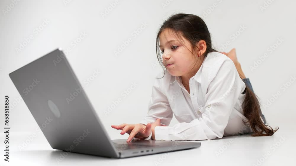 Cute, happy girl studying online using a laptop. Concept of a happy child studying online on a light background. Cute, happy girl studying online using a laptop. Concept of a happy child studying online on a light background.