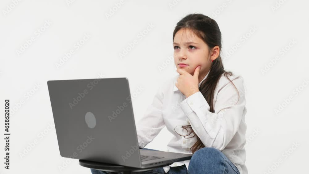 Idea concept. A cute little girl in front of a laptop experiences emotions from an idea or solution to a problem, the girl uses a computer for distance learning on a light background. Idea concept. A cute little girl in front of a laptop experiences emotions from an idea or solution to a problem, the girl uses a computer for distance learning on a light background.