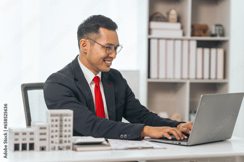 Agent presents contracts for property purchase or lease. Businessman asian indian people showcases miniature model home, signifying secure property insurance. Desk scene in a home sales office. Agent presents contracts for property purchase or lease. Businessman asian indian people showcases miniature model home, signifying secure property insurance. Desk scene in a home sales office.