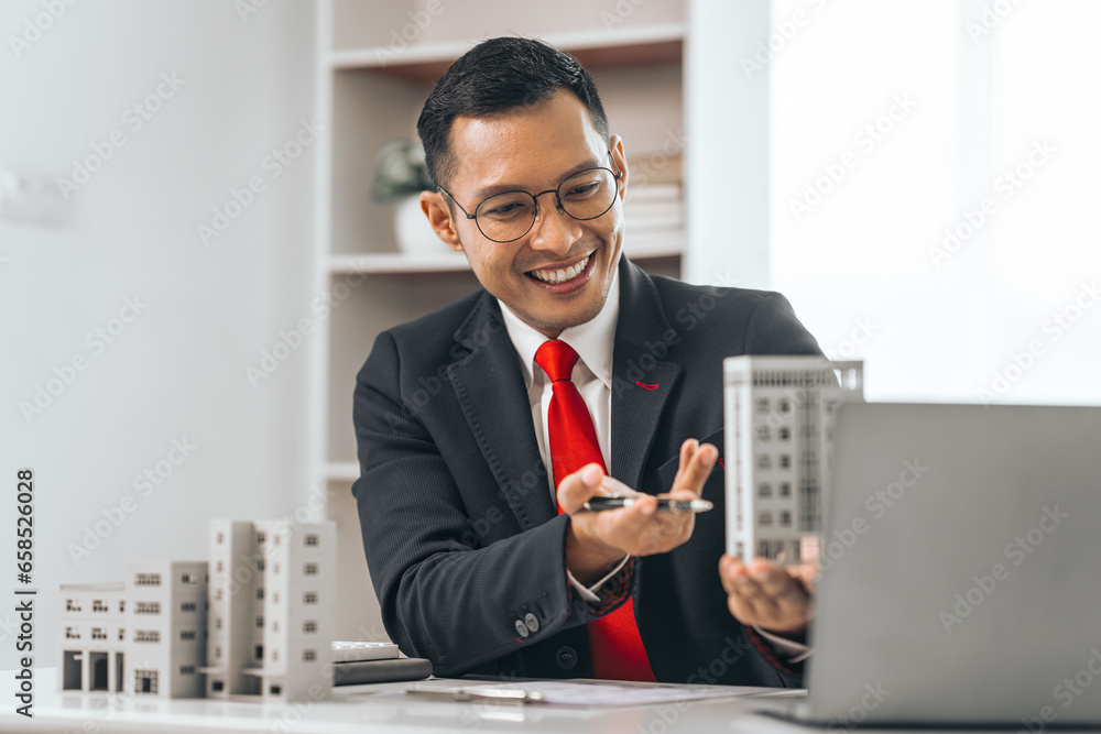 Agent presents contracts for property purchase or lease. Businessman asian indian people showcases miniature model home, signifying secure property insurance. Desk scene in a home sales office.