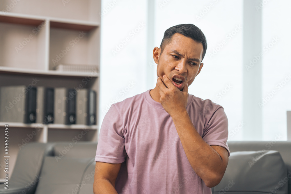 Naklejka premium Middle-aged Asian Indian man with gum disease, toothache, wisdom tooth and molar pain. sitting on the sofa