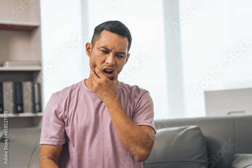 Middle-aged Asian Indian man with gum disease, toothache, wisdom tooth and molar pain. sitting on the sofa