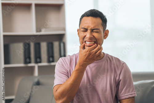 Middle-aged Asian Indian man with gum disease, toothache, wisdom tooth and molar pain. sitting on the sofa