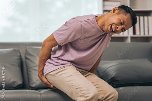 Bild auf Leinwand Middle-aged Asian Indian man with butt pain, hemorrhoids, colon pain, sitting on a sofa