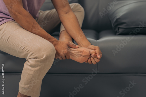 Middle-aged Asian Indian man with ankle disease, plantar pain, sitting on the sofa.