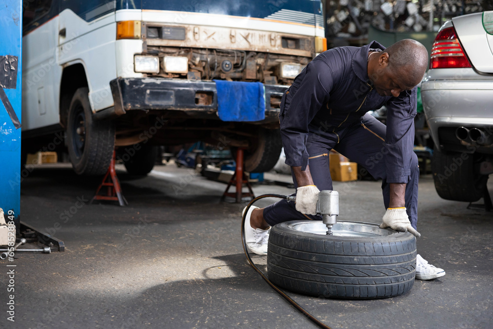 African mechanic worker fixing tire with old car in garage
