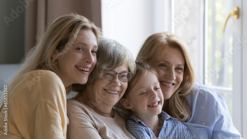 Happy cute female relatives posing for camera with toothy smiles, looking away, sitting close on home sofa, hugging with love, meeting due to 8 march, mothers day. Family portrait, banner shot