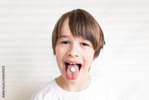 Happy boy puts the pill into his mouth. Close up portrait of child with pill on hes tongue at home ,taking medicine, taking vitamins,medical, nutrition, healthcare concept