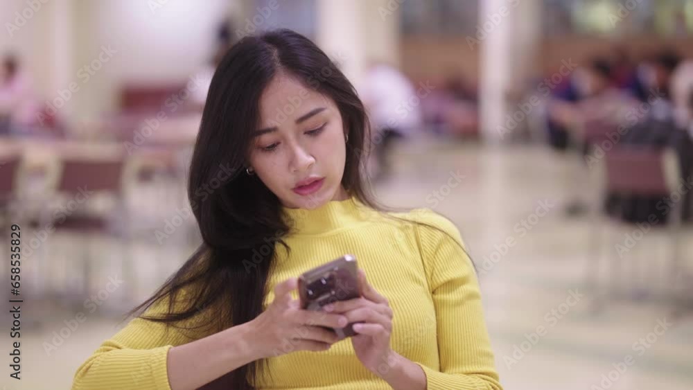 nice Asian student woman sitting at table and using cellphone or smartphone texting chatting social media or listening song while doing homework in library or reading room. nice Asian student woman sitting at table and using cellphone or smartphone texting chatting social media or listening song while doing homework in library or reading room.