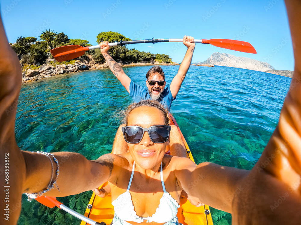 Φωτογραφία Overjoyed couple of caucasian adult tourist man and woman taking selfie picture inside a kayak canoe with blue clean sea ocean water and coastline in background