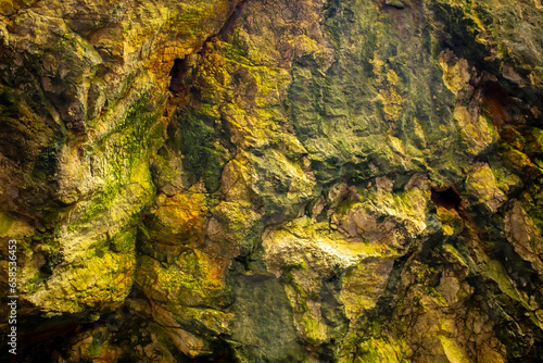Natural rock texture background. Rocky bas-relief wall. Green moss on the surface of the rocks.