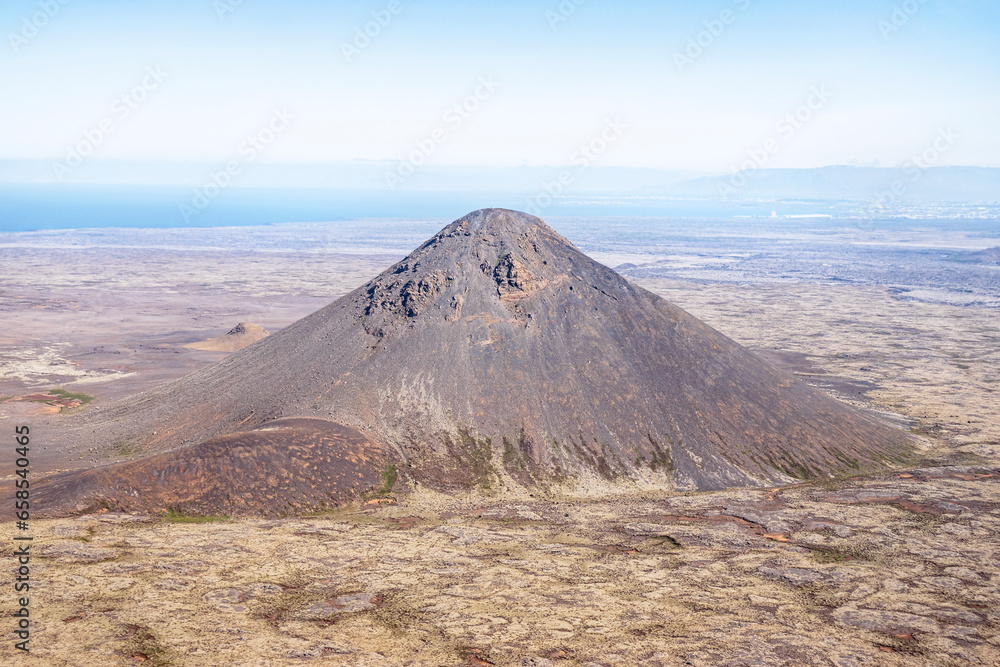aerial view of a small volcanic cone lava formation in the Fagradalsfjall volcano area near the Litli-Hrutur eruption on the Reykjanes peninsula in Iceland with a hazy blue sky in the background