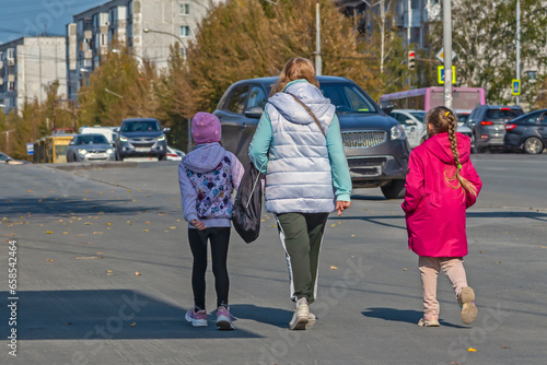 Mother and daughters walk on the sidewalk on an autumn day